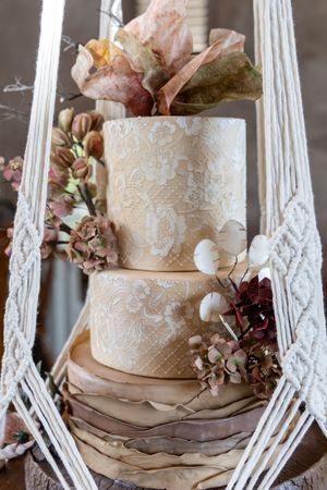 Elegant three-tier wedding cake with delicate lace details and burgundy floral accents displayed on white vintage stand.