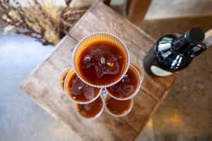 Several cups of amber-colored craft beer arranged in a floral pattern on a wooden surface from above.