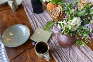 Rustic table setting with plates, wine glasses, and fresh greenery centerpieces at a restaurant or dining event.
