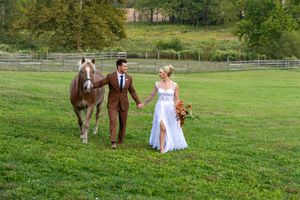 A couple in wedding attire walks hand in hand through a peaceful green field on their special day.