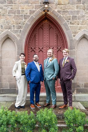 Group standing against stone church wall with red gothic doorway and green shrubbery.