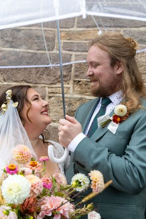 A couple shares a joyful moment under a clear umbrella with colorful flowers in the foreground.