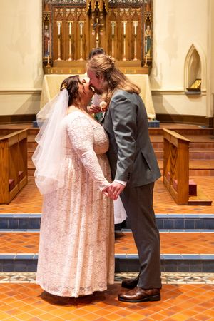 Couple sharing a romantic moment in church aisle with wooden pews and terracotta flooring.