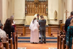 A religious ceremony takes place inside a church sanctuary with people gathered around the altar area.