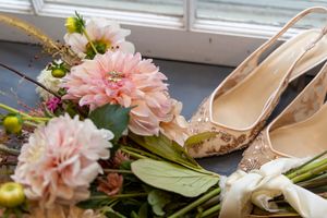Elegant blush pink floral arrangement with gold accents and cream colored high heel shoes arranged on a table.