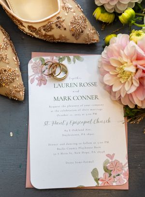 Wedding invitation with pink floral design and gold accents displayed with flowers.