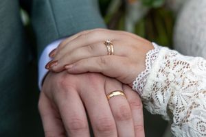 Close-up view of hands wearing wedding rings with delicate white lace details in the background.