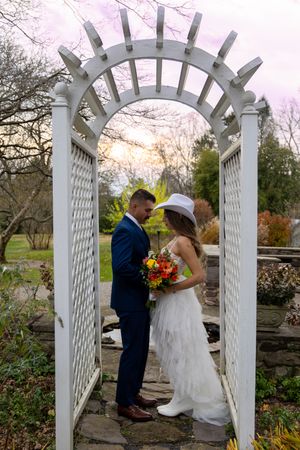 A couple shares a romantic moment under a white garden arbor during their outdoor wedding celebration.