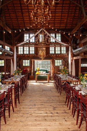 Rustic barn venue interior with wooden floors, chandeliers and long tables set for an elegant event.