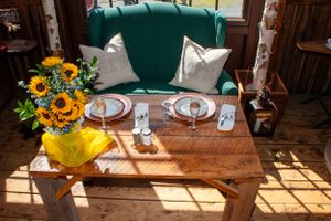 Table setting with green velvet seating and sunflower centerpiece in sunlit rustic room.