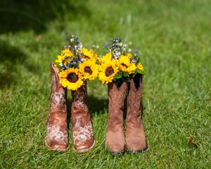 Two pairs of cowboy boots filled with bright sunflowers sitting on green grass.