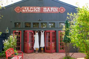 Two white wedding dresses hanging outside red doors of Jack's Barn rustic wedding venue.