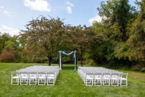 White chairs set up for outdoor wedding ceremony with blue arch on green lawn.