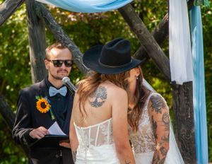 A wedding ceremony outdoors with sunflowers and tattoos visible on the bride's back.