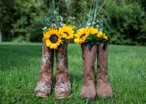 Two pairs of cowboy boots filled with sunflowers sitting on green grass.