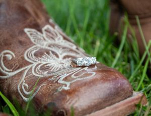 Diamond ring displayed on embroidered brown leather cowboy boot in grass.