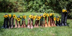 A line of brown boots and rain boots with sunflowers arranged on grass for a wedding photo.