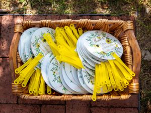 Wicker basket filled with yellow plastic utensils and floral patterned paper plates.