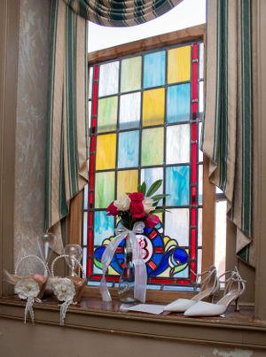 Colorful stained glass window with red roses and bridal shoes on windowsill in historic inn setting.