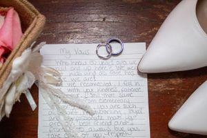 Wedding rings rest on handwritten vows next to white bridal shoes.