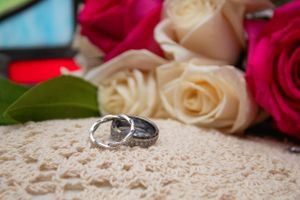 Wedding rings displayed on lace fabric with pink and white roses in background.