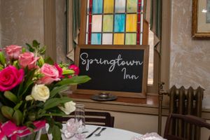 Springlawn Inn chalkboard sign under decorative stained glass window with fresh floral arrangements.