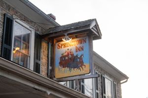 Illuminated vintage Springlawn Inn sign featuring stagecoach artwork mounted on building exterior.