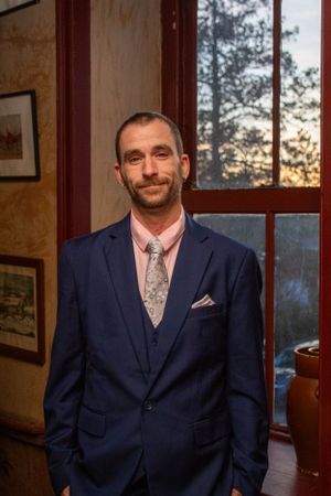 Professional portrait in elegant navy suit against window with sunset view.