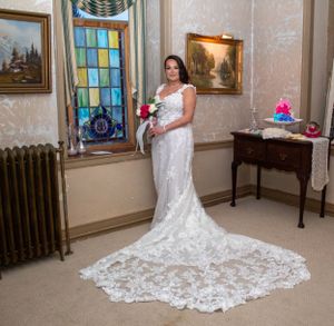 Elegant bridal portrait featuring intricate lace wedding gown with cathedral train in historic setting.