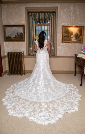 Back view of lace wedding gown with dramatic cathedral train in historic room setting.