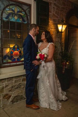 Wedding couple beside stained glass window at historic stone venue with outdoor lantern.