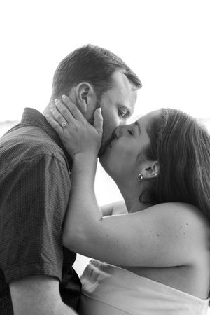 Black and white photo of a couple sharing a romantic kiss, woman tenderly holding man's face with both hands.