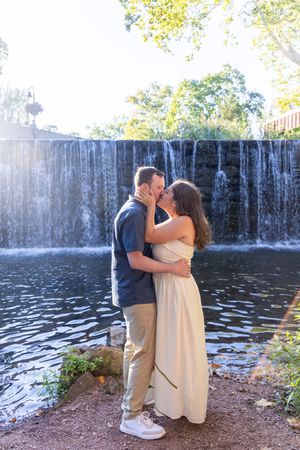 Couple sharing a romantic kiss in front of a cascading waterfall, woman in white dress, man in blue shirt.