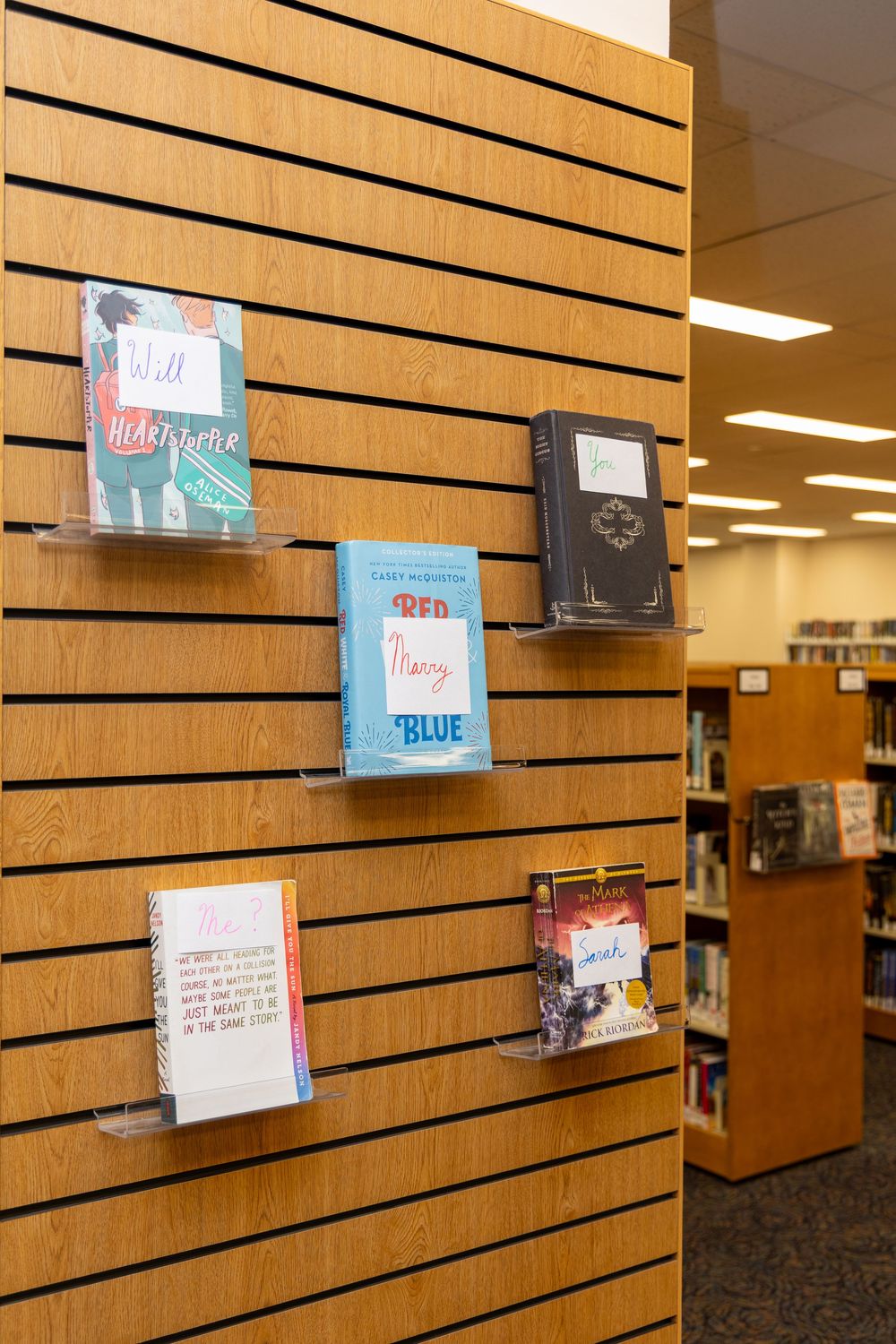 Books displayed on wall-mounted clear acrylic shelves in a modern library or bookstore setting.