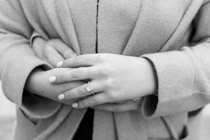 Black and white close-up photo of hands with an engagement ring crossed over a light colored sweater.