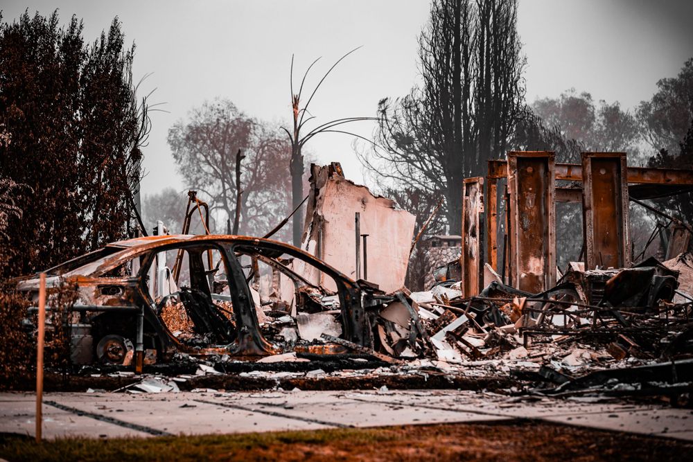 Charred remains of a burned down building with collapsed walls and debris against a moody sky.
