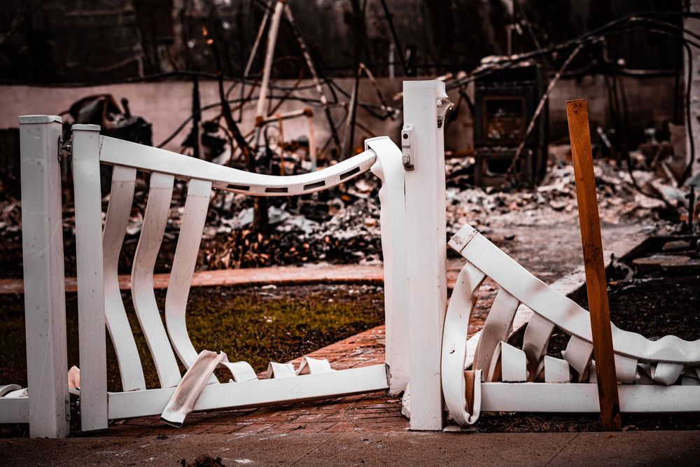 Damaged white fence among debris and ashes from fire destruction.