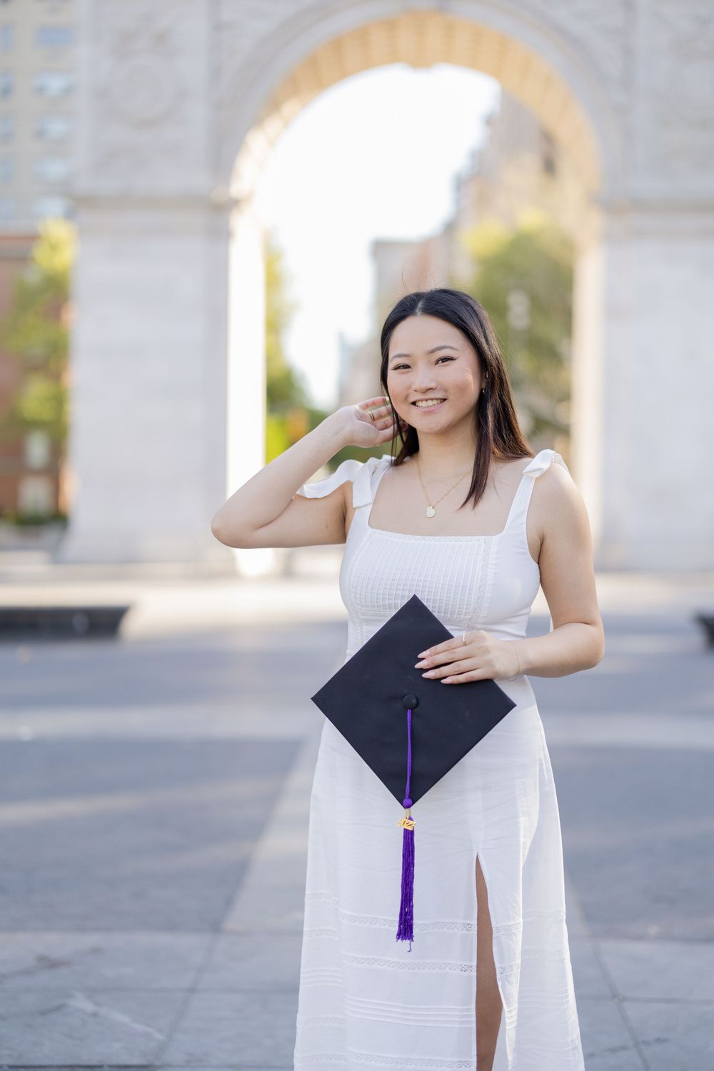 Graduate poses with graduation cap against stone architecture background.