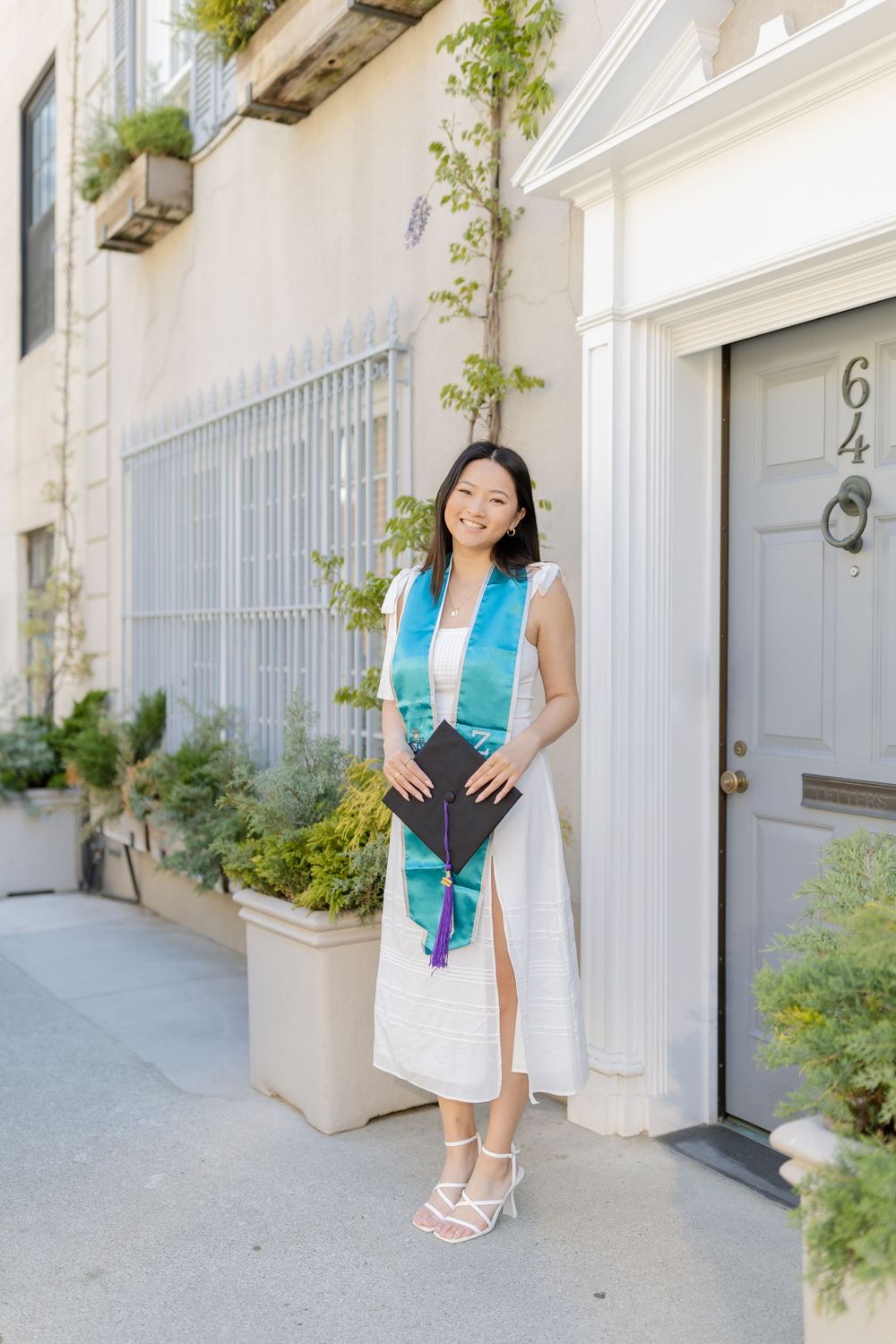 Graduate in white dress and blue stole poses elegantly outside door number 64.