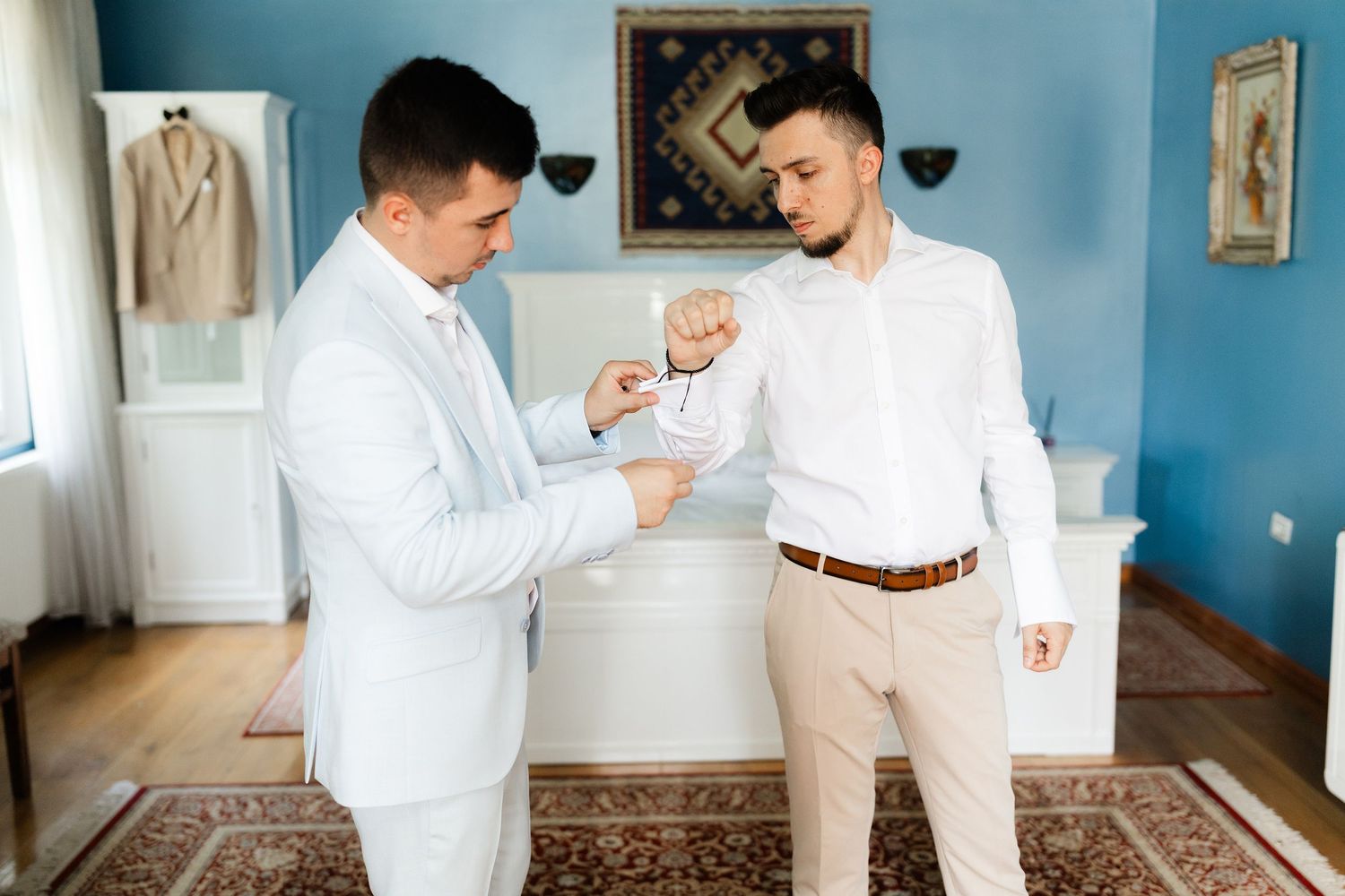 A couple in white outfits dance together in a blue-walled room with elegant decor and natural lighting.