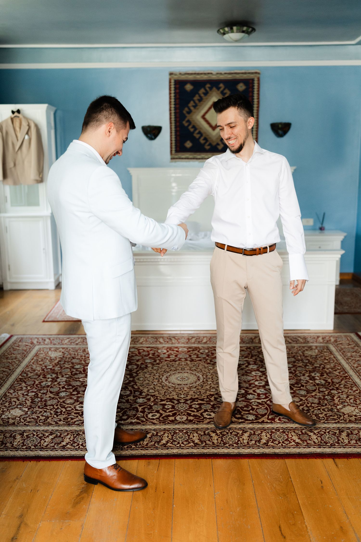 Two people in contrasting outfits, one in white and one in khaki, dance together on a hardwood floor with an ornate rug.