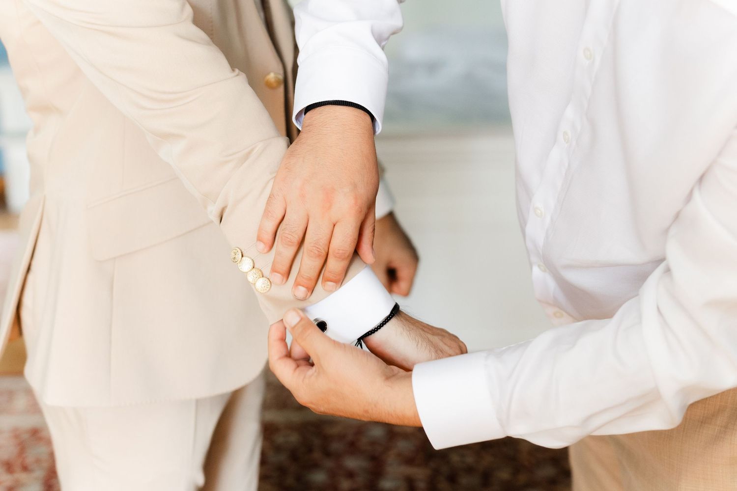 Close-up view of hands adjusting a white cuff link on a formal dress shirt sleeve.