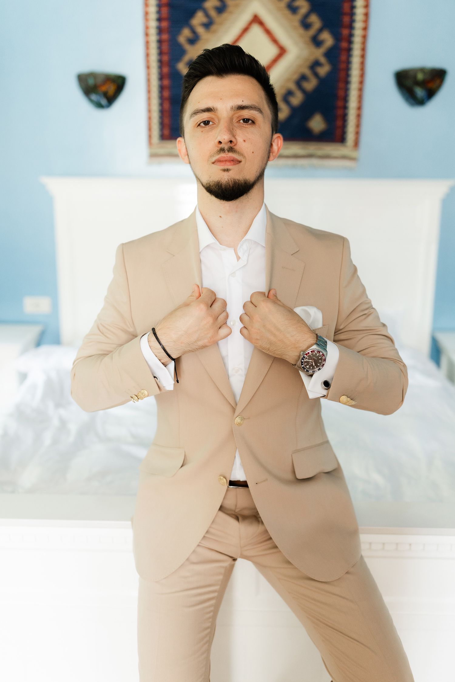 A person in a beige suit strikes different poses against a light blue wall with decorative wall art.