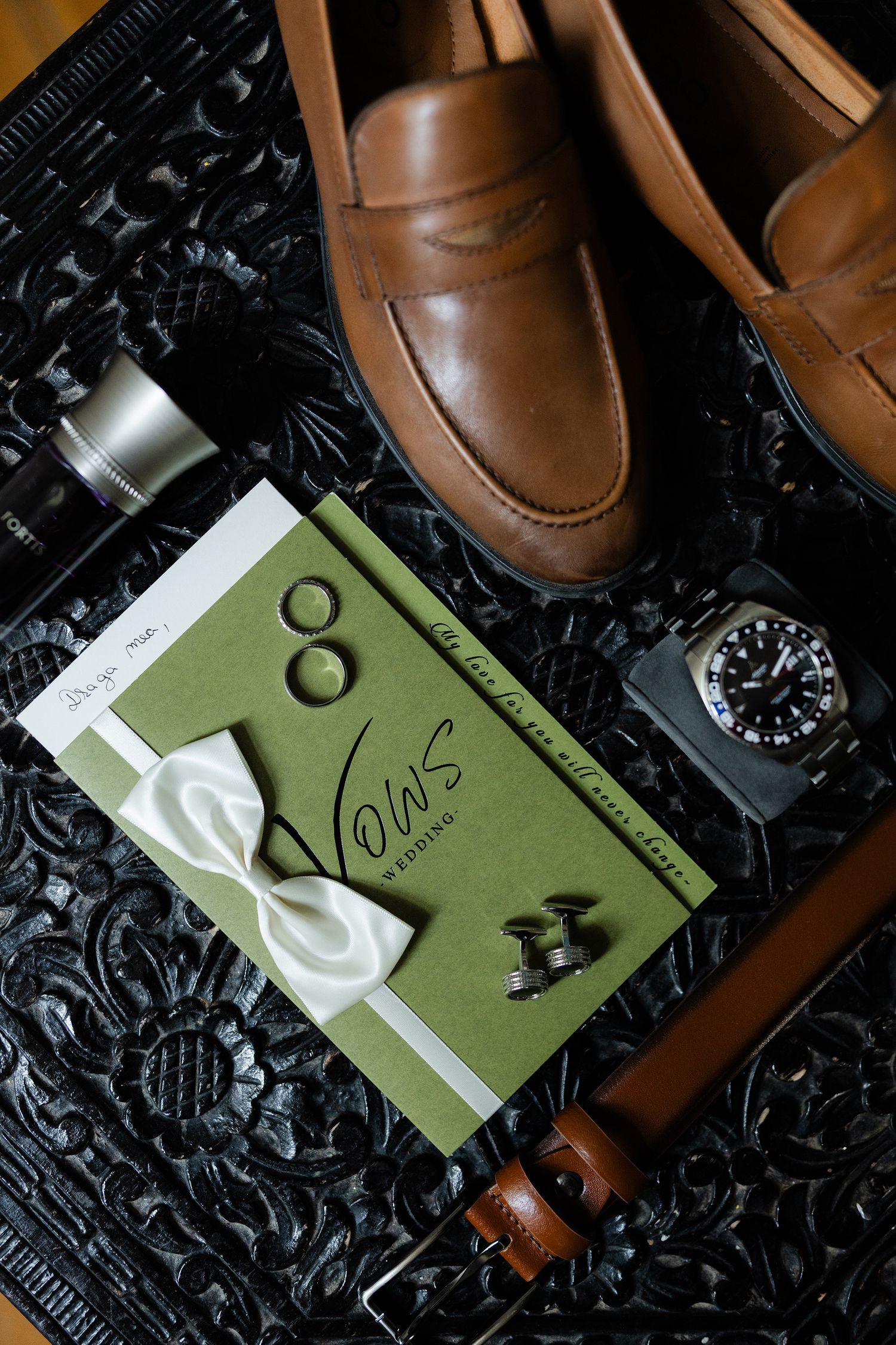 Stylish brown leather shoes arranged with a green card and watch on a dark textured background.