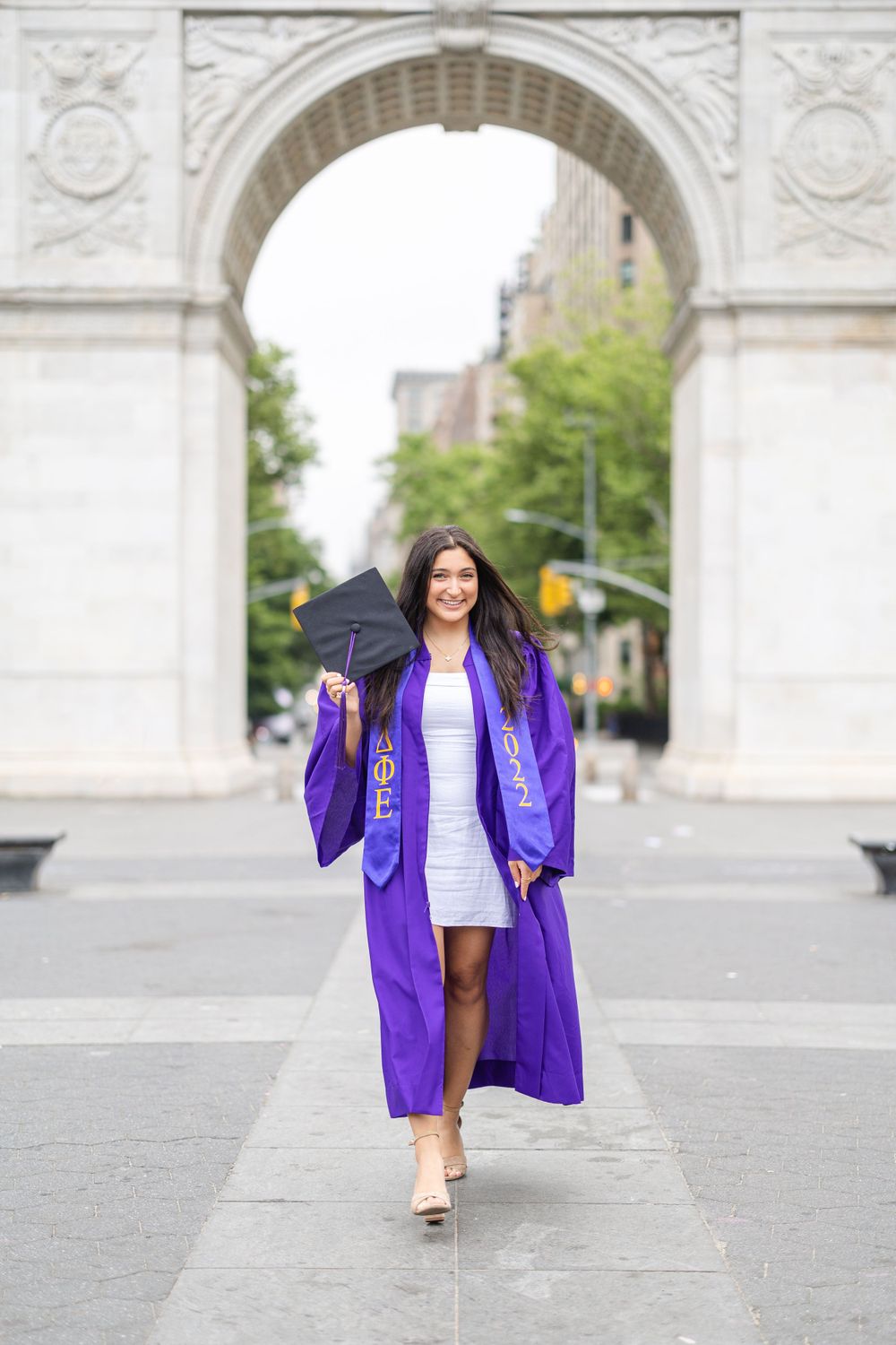 Graduate walking through Washington Square Arch wearing purple graduation gown and regalia.