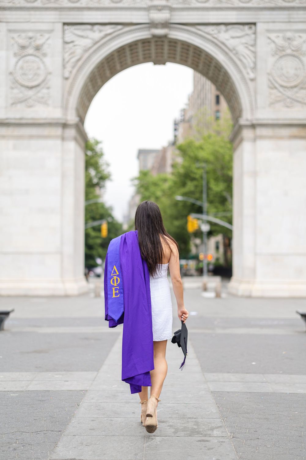 Graduate walking away from Washington Square Arch in purple graduation gown.