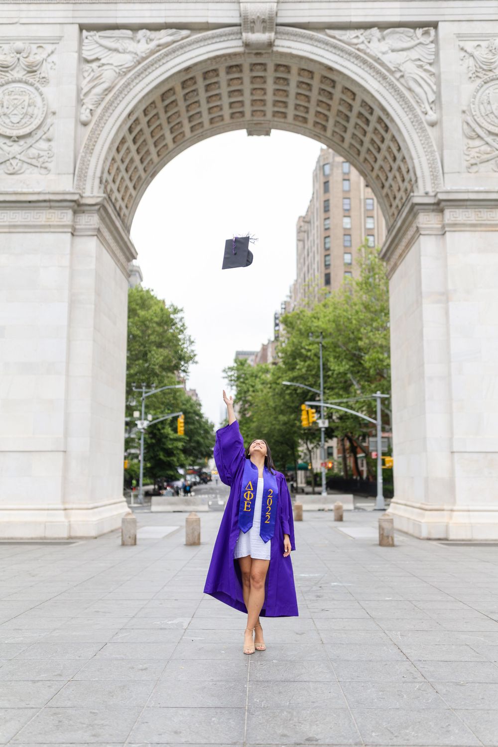 Graduate tosses cap in celebratory pose under Washington Square Arch.