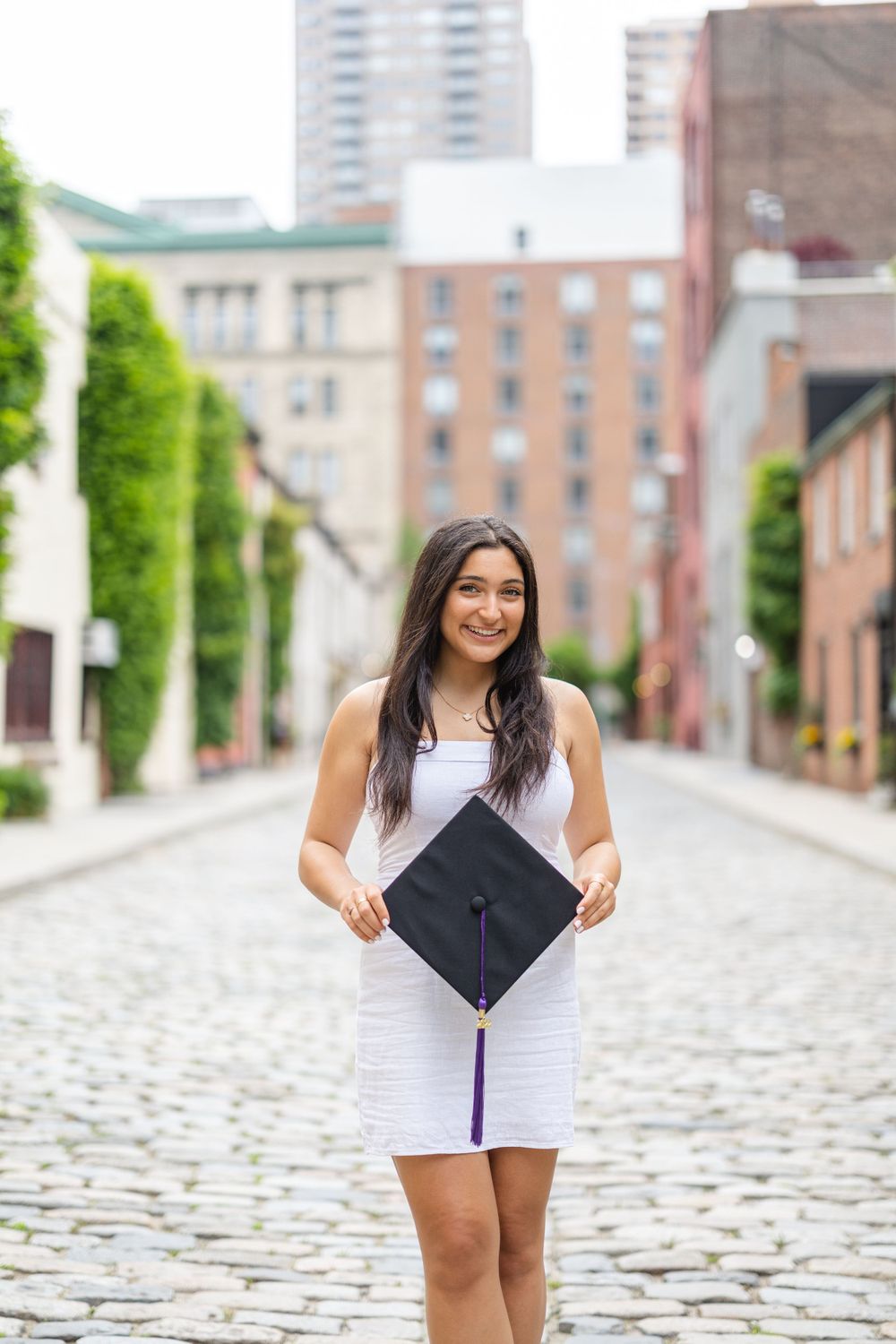 Graduate holding decorated graduation cap on cobblestone street.