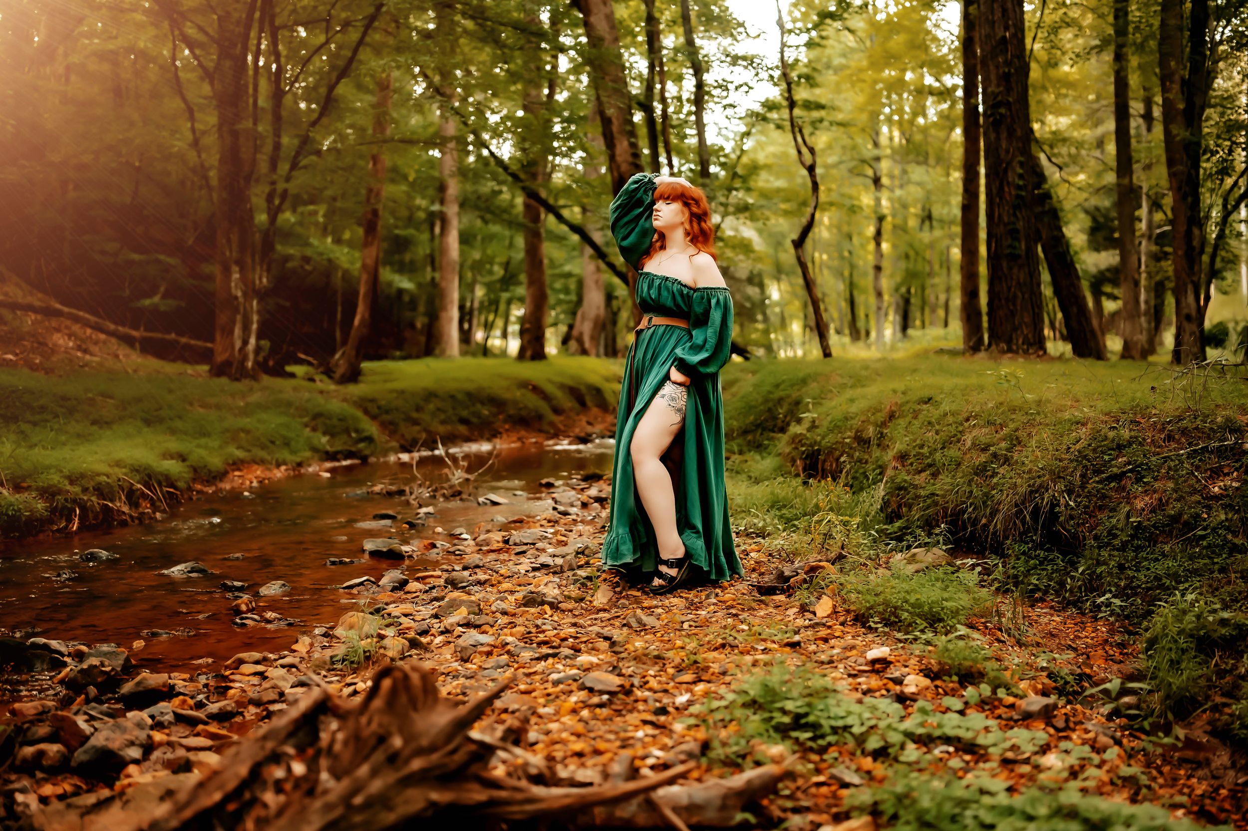 A figure in a green jacket walks along a winding forest path covered in autumn leaves at sunset.