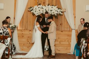 Bride and groom exchanging rings at floral arch altar in rustic barn wedding ceremony.